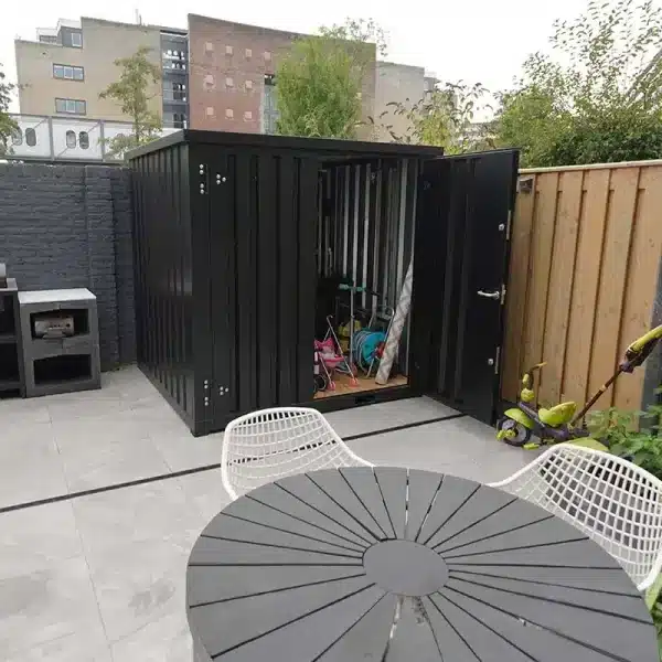Zwarte demontabele opslagcontainer in stadstuin voor opbergen van tuinspullen en kinderspeelgoed.