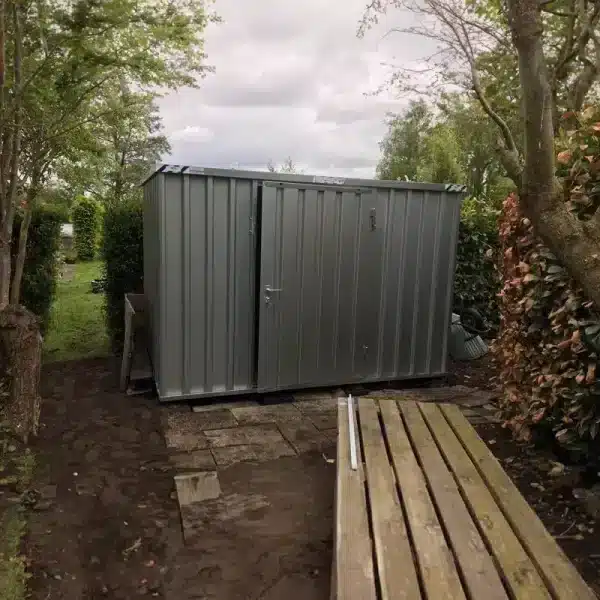BOS opslagcontainer van verzinkt staal geplaatst in een tuinpad tussen bomen en hagen