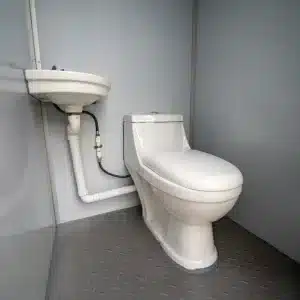 Binnenkant van een prefab toiletunit met keramisch toilet en wastafel.