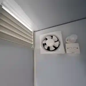 Ventilatiesysteem in prefab toiletunit met mechanische afzuiging en natuurlijke luchtroosters.