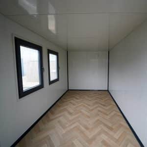 Interieur van een kantoorunit 4x2 meter met houtlook vloer, witte wanden en twee ramen voor natuurlijk licht.