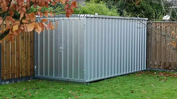 Verzinkte snelbouwcontainer geplaatst in een hoek van de tuin met houten schutting